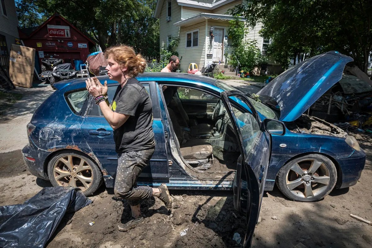 a woman is standing next to a blue car in the mud.