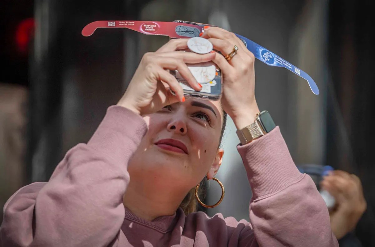 Woman in pink hoodie looking through a pinhole projector to view a solar eclipse.