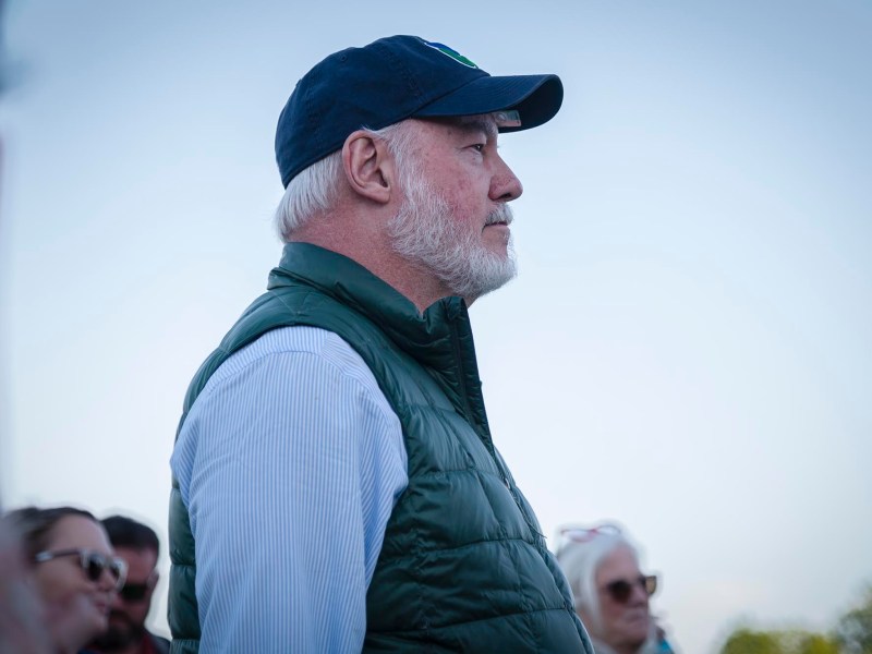 a man wearing a hat and vest standing next to a group of people.