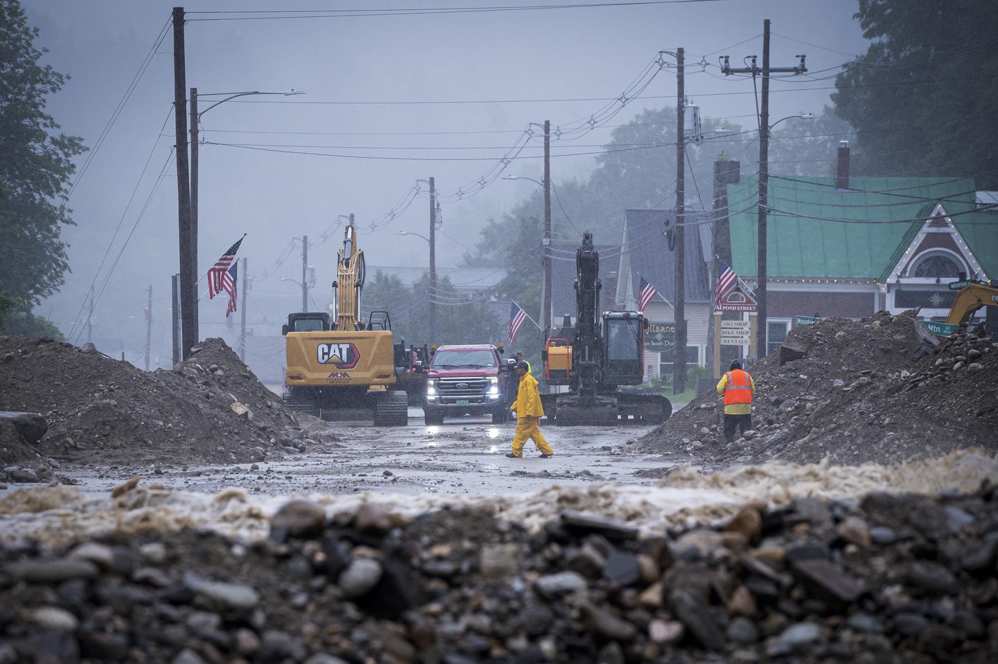 a man in a yellow raincoat walks through a flooded street.