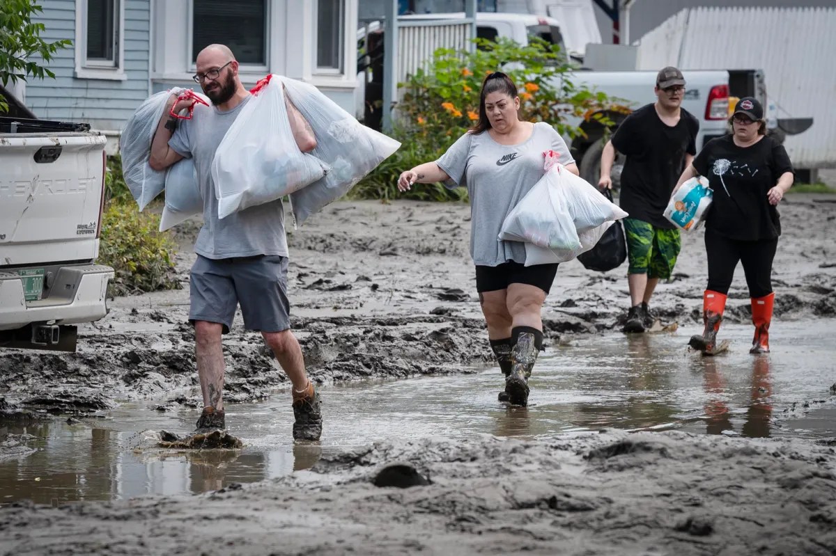 a group of people carrying bags through a muddy street.