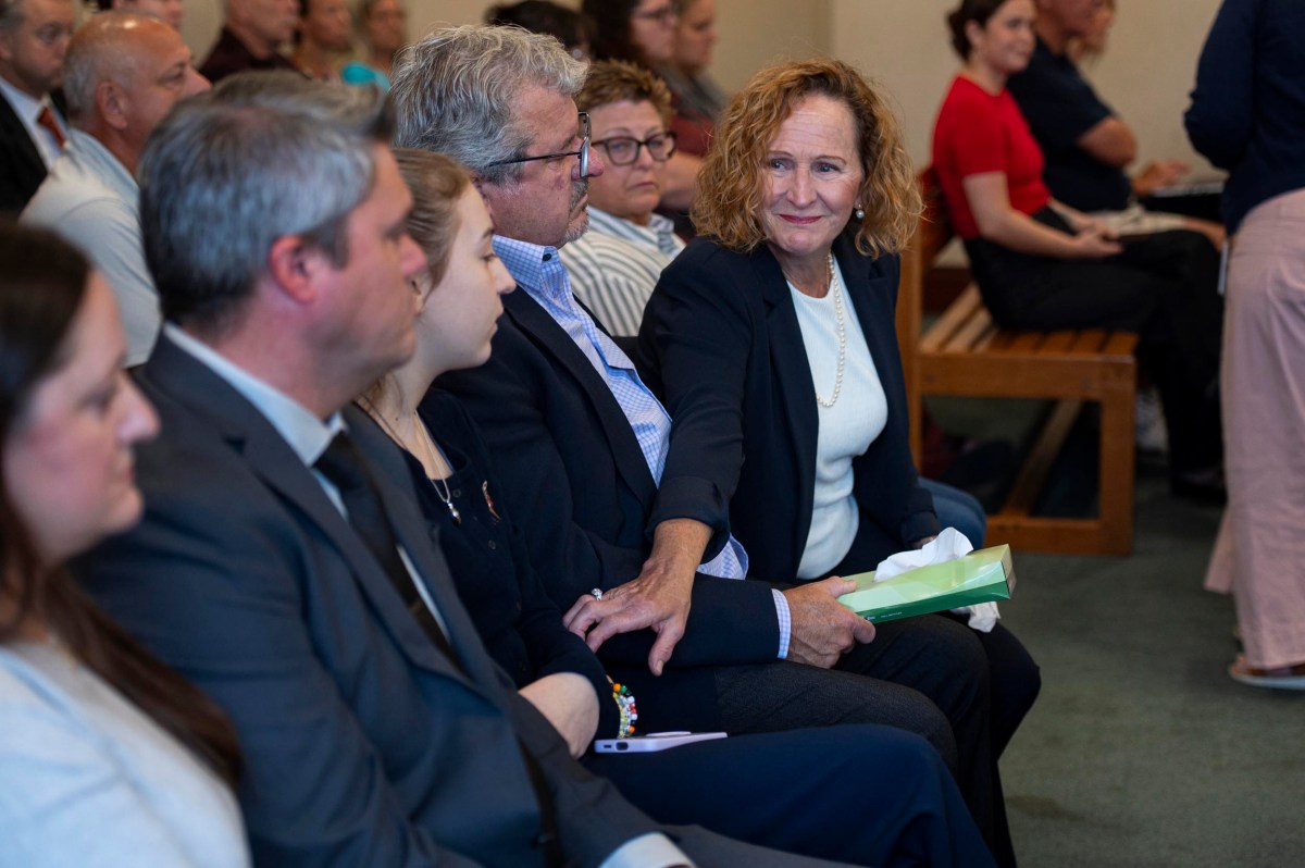 A woman sitting among a group of people touches a man's hand and holds a box of tissues, while others sit attentively in the background.