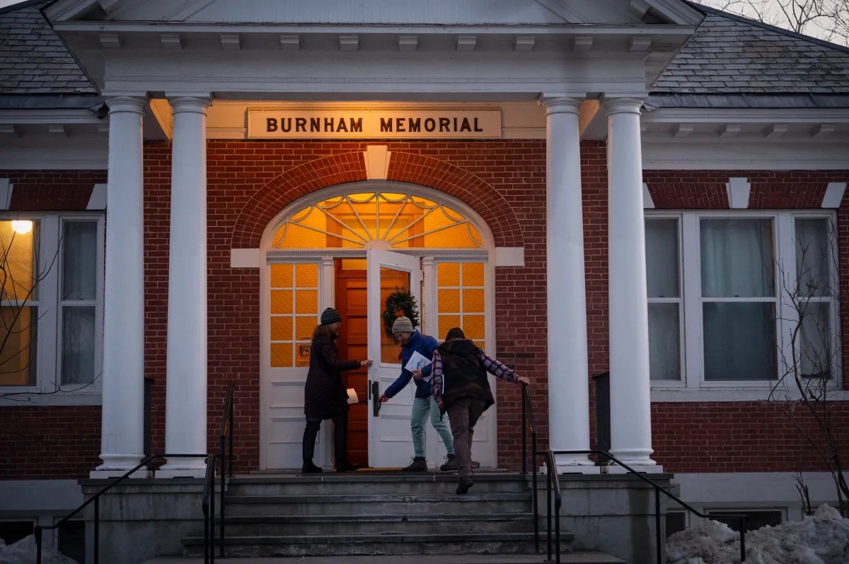 Three people entering Burnham Memorial building through an open door, ascending a short flight of steps.