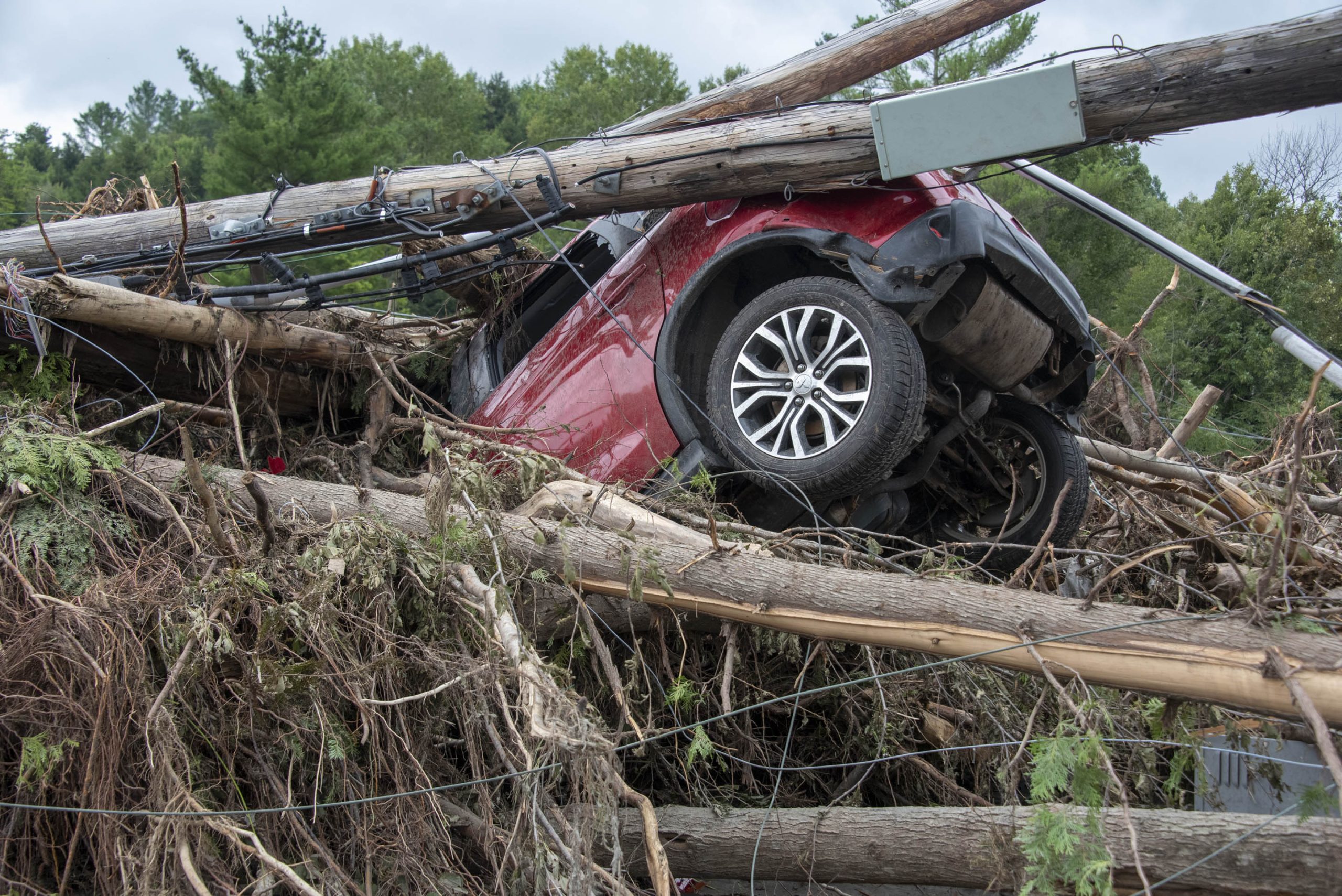 A red SUV is overturned and entangled in fallen trees and debris after a severe storm.