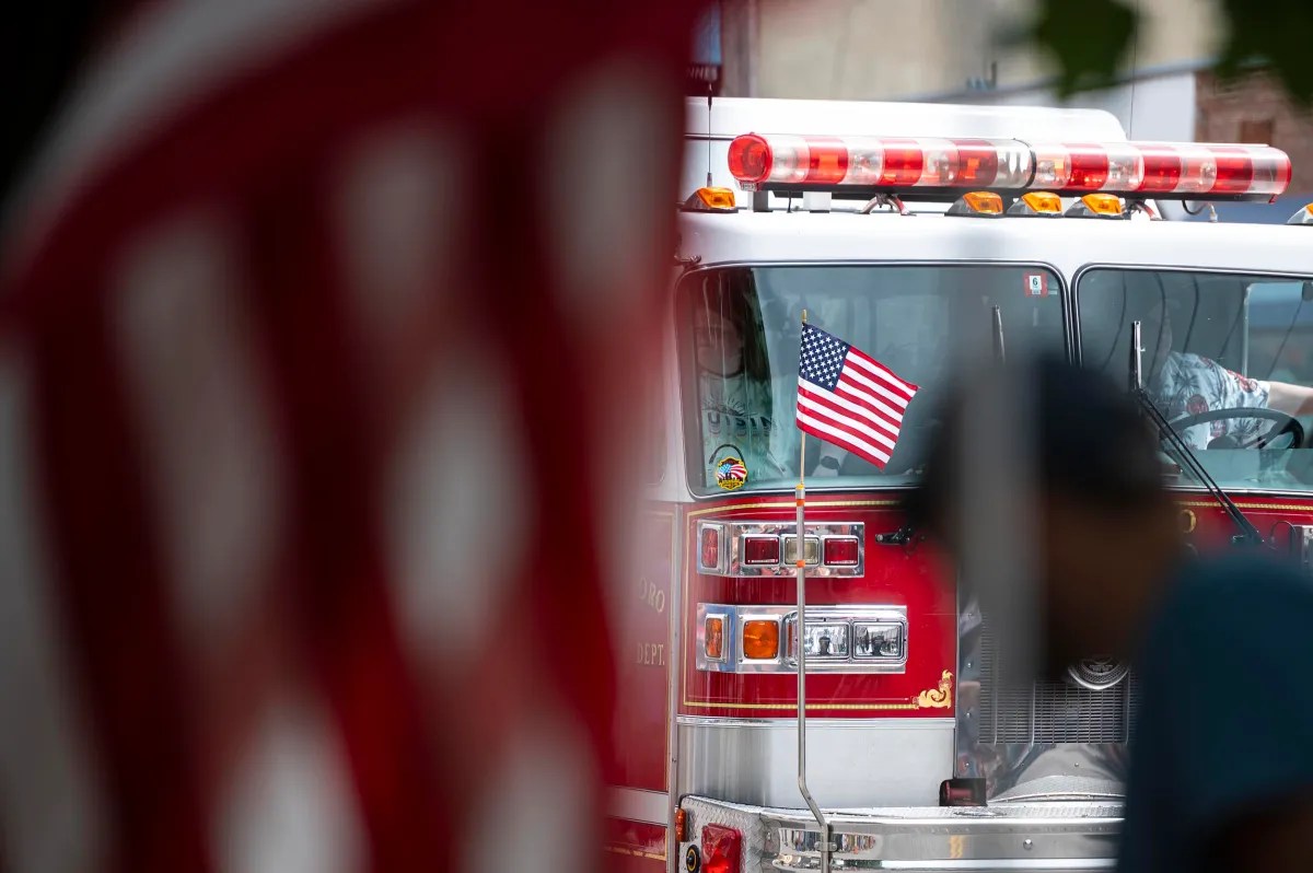 A fire truck with an American flag on the front visible amid a blurred foreground and silhouetted figure.