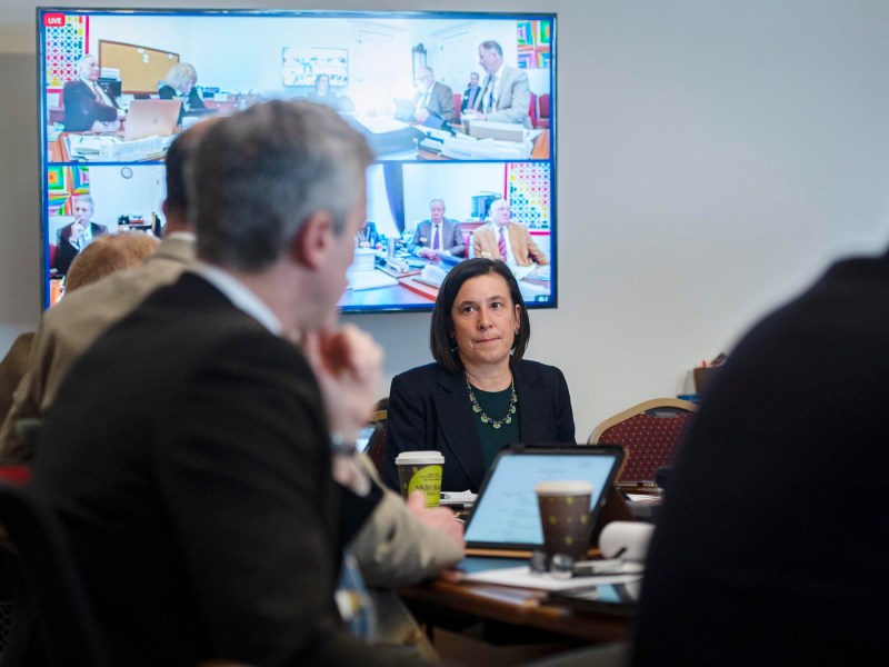 People sitting around a conference table with a screen displaying a video call in a meeting room.
