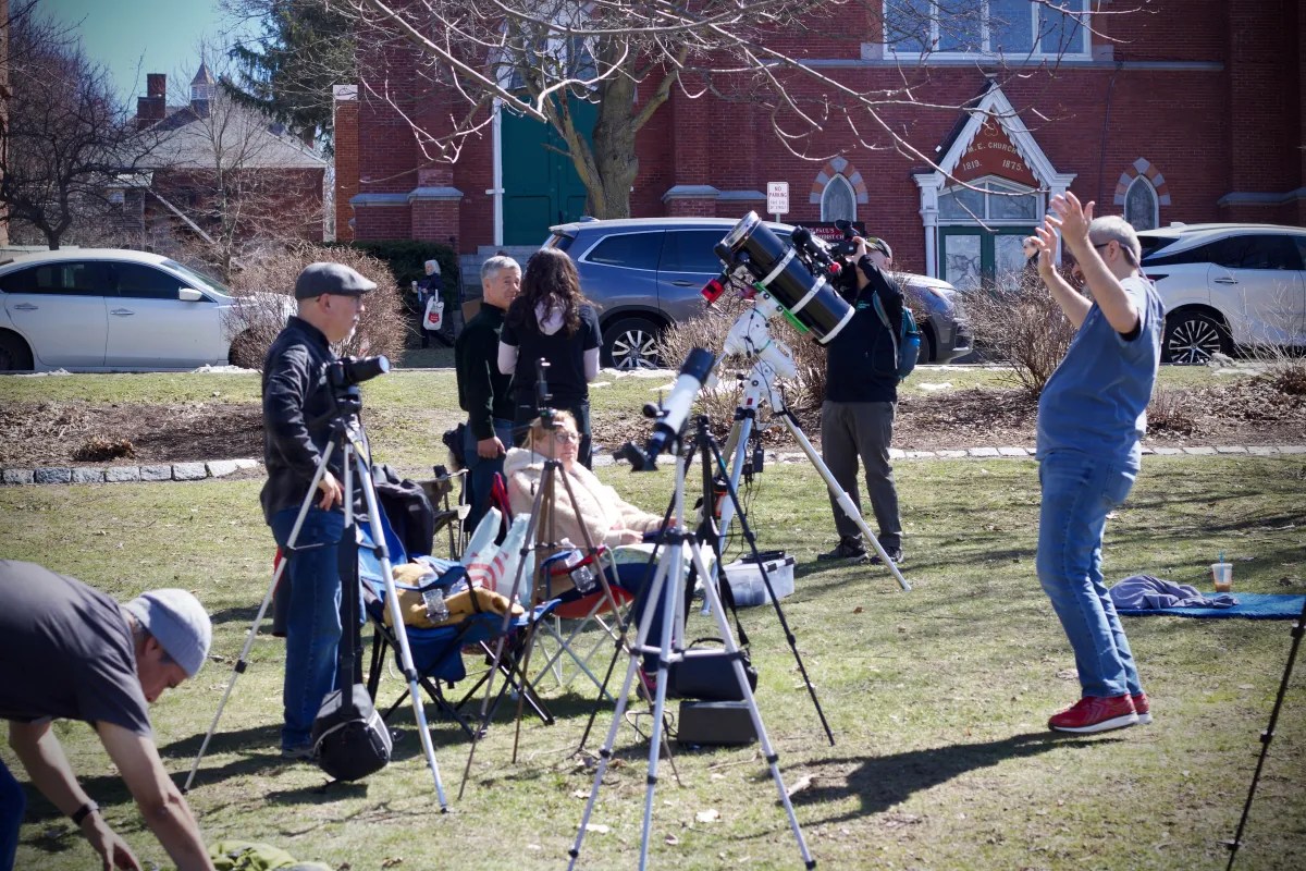 People stand on grass among telescopes and camera tripods.